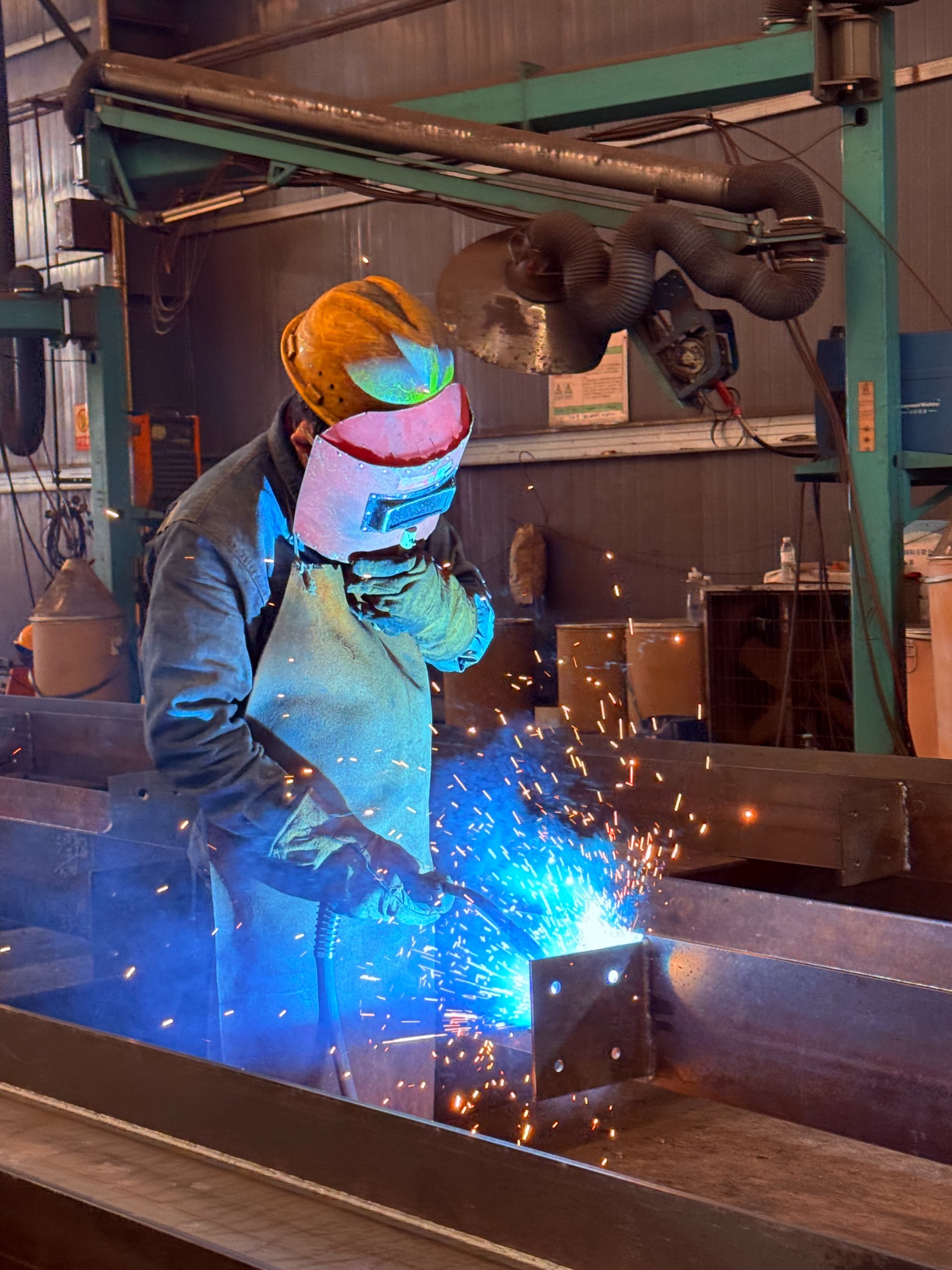 Welder fabricating a structural steel member in the workshop
